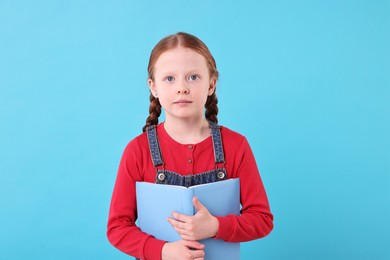 Photo of Cute girl with book on light blue background