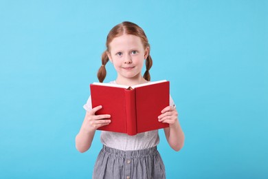 Cute girl with book on light blue background