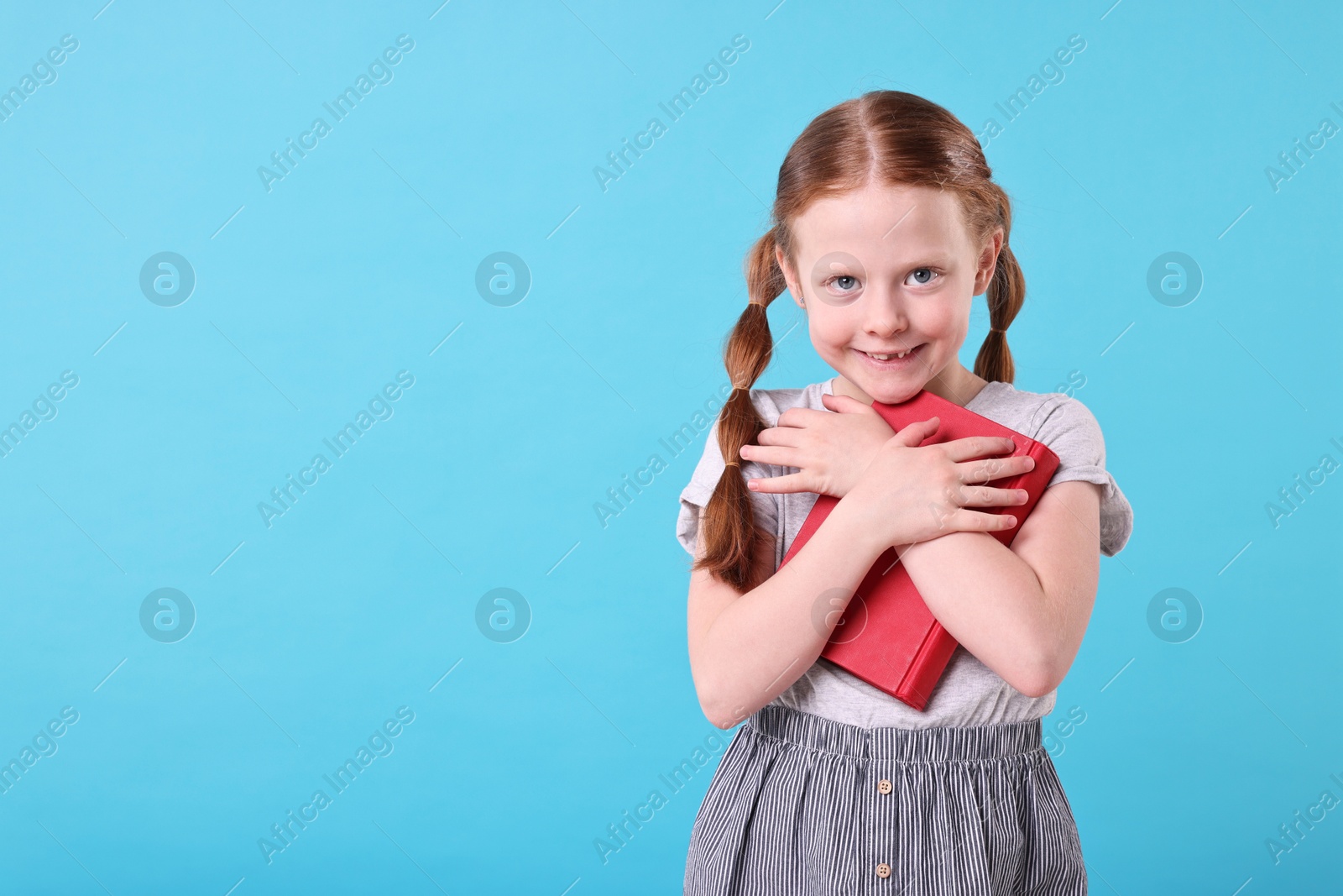 Photo of Smiling girl with book on light blue background. Space for text