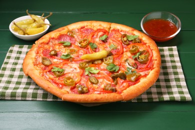 Photo of Delicious pizza Diablo, sauce and pickled peppers on green wooden table