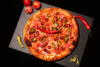 Photo of Slate board with delicious pizza Diablo, tomatoes and peppers on black background, top view