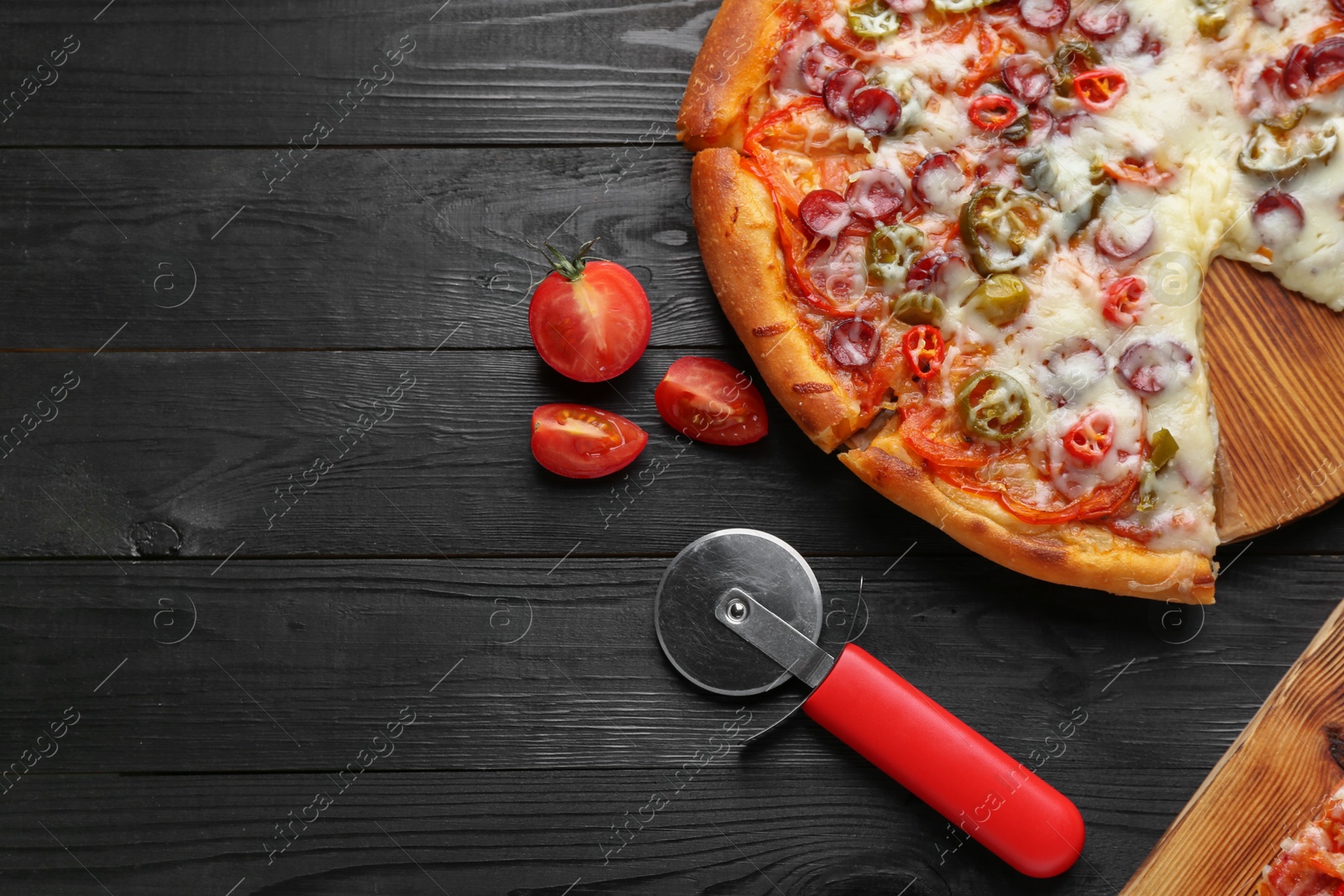 Photo of Delicious pizza Diablo, tomatoes and cutter on black wooden table, flat lay. Space for text