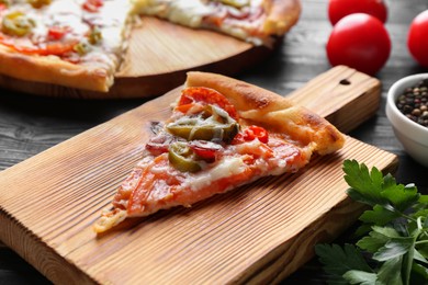 Photo of Wooden board with delicious pizza Diablo and parsley on black table, closeup