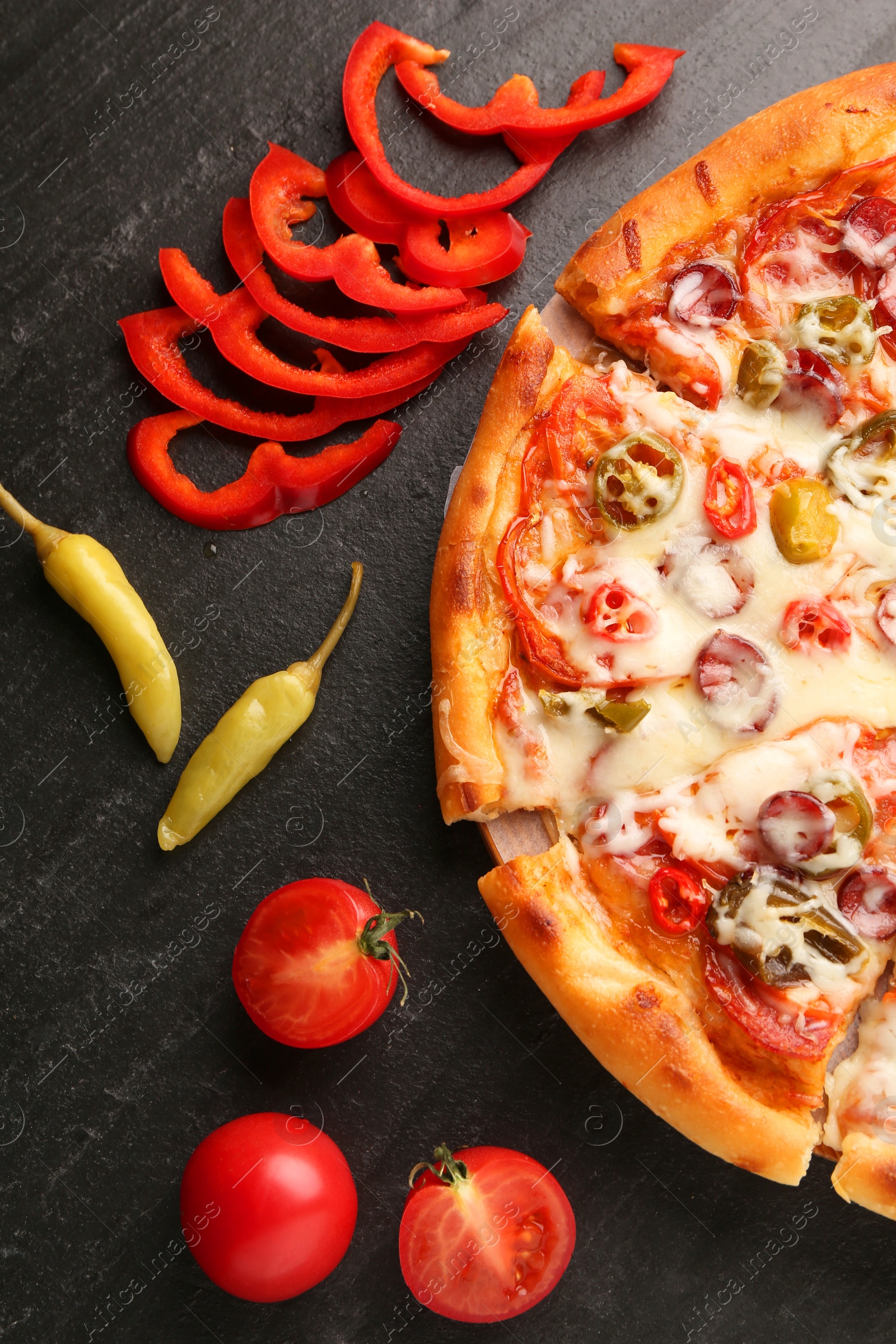 Photo of Delicious pizza Diablo, tomatoes and peppers on dark textured table, flat lay