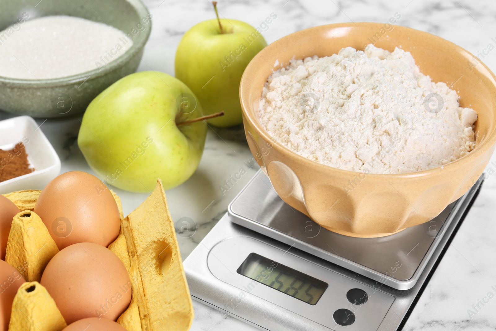 Photo of Kitchen scale with bowl of flour and products on white marble table, closeup