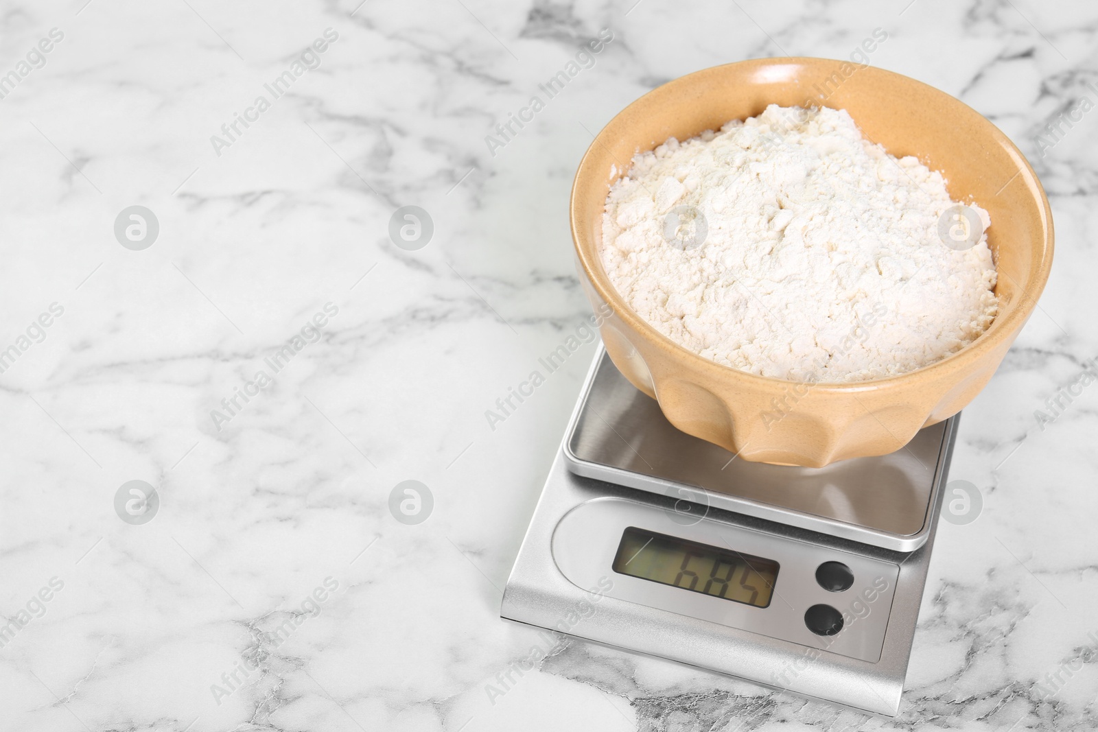 Photo of Kitchen scale with bowl of flour on white marble table, closeup. Space for text