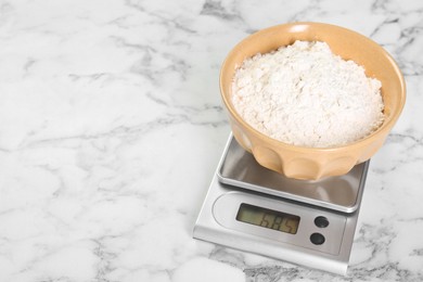 Photo of Kitchen scale with bowl of flour on white marble table, closeup. Space for text