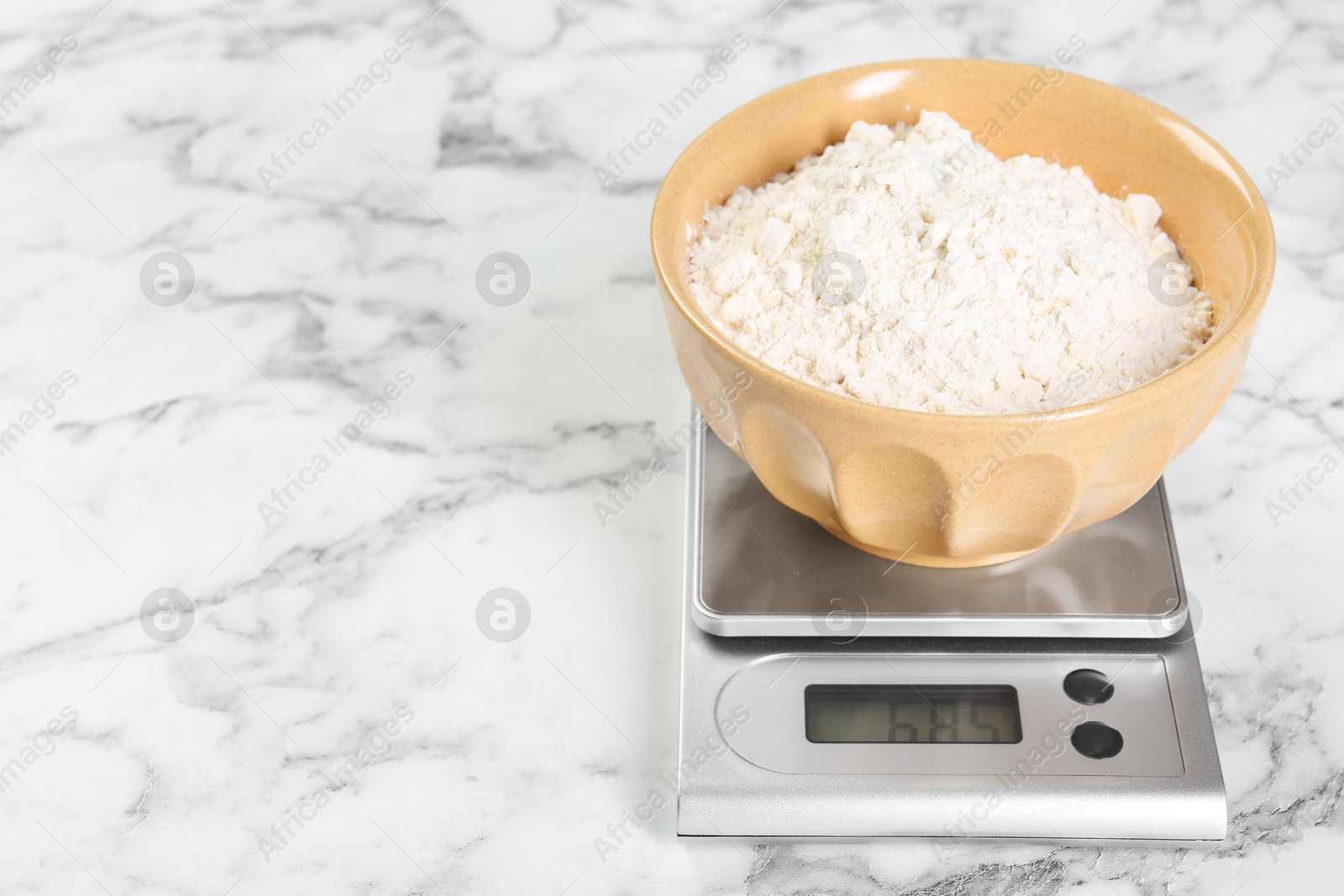 Photo of Kitchen scale with bowl of flour on white marble table, closeup. Space for text