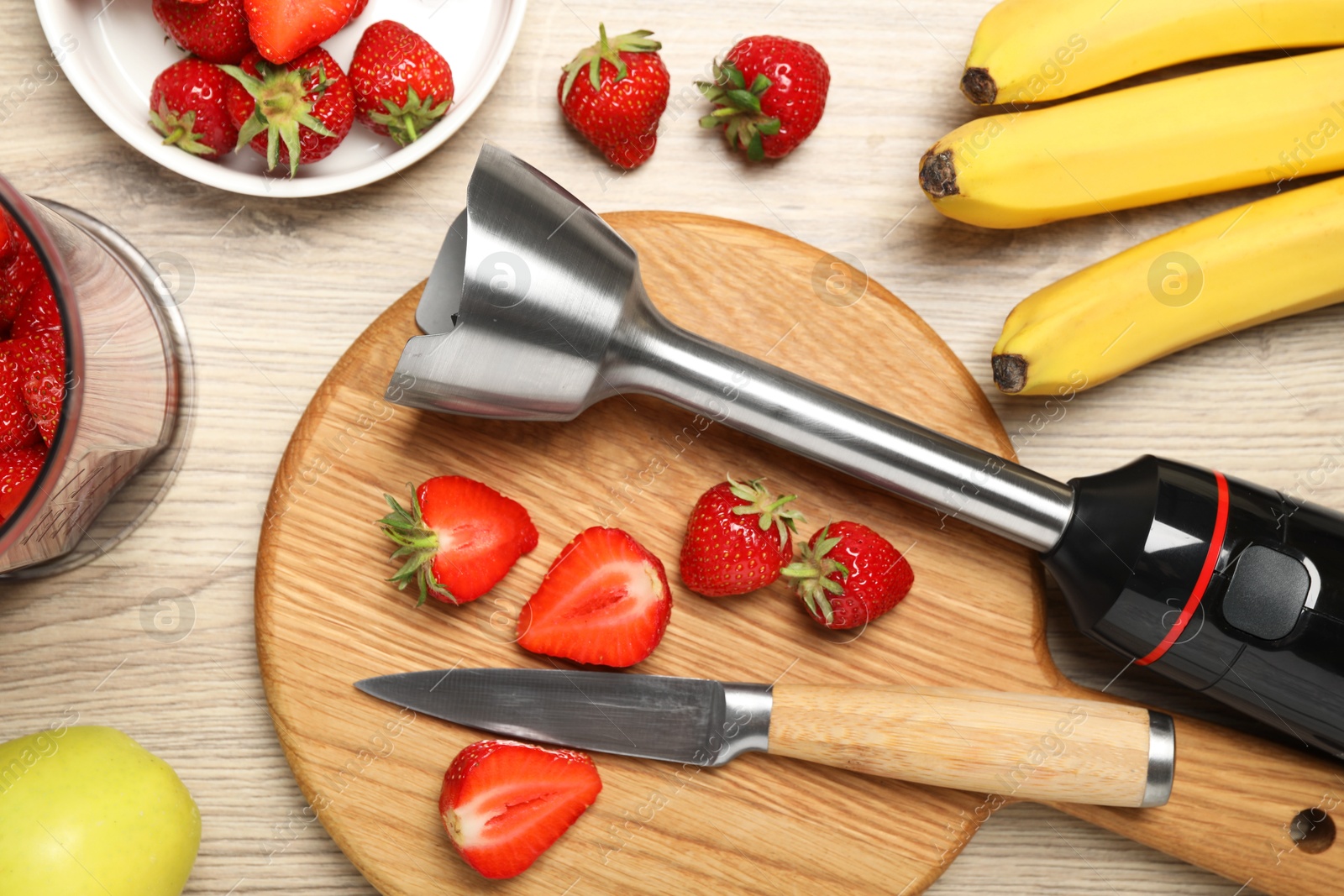 Photo of Hand blender kit, fresh bananas, strawberries and knife on wooden table, flat lay