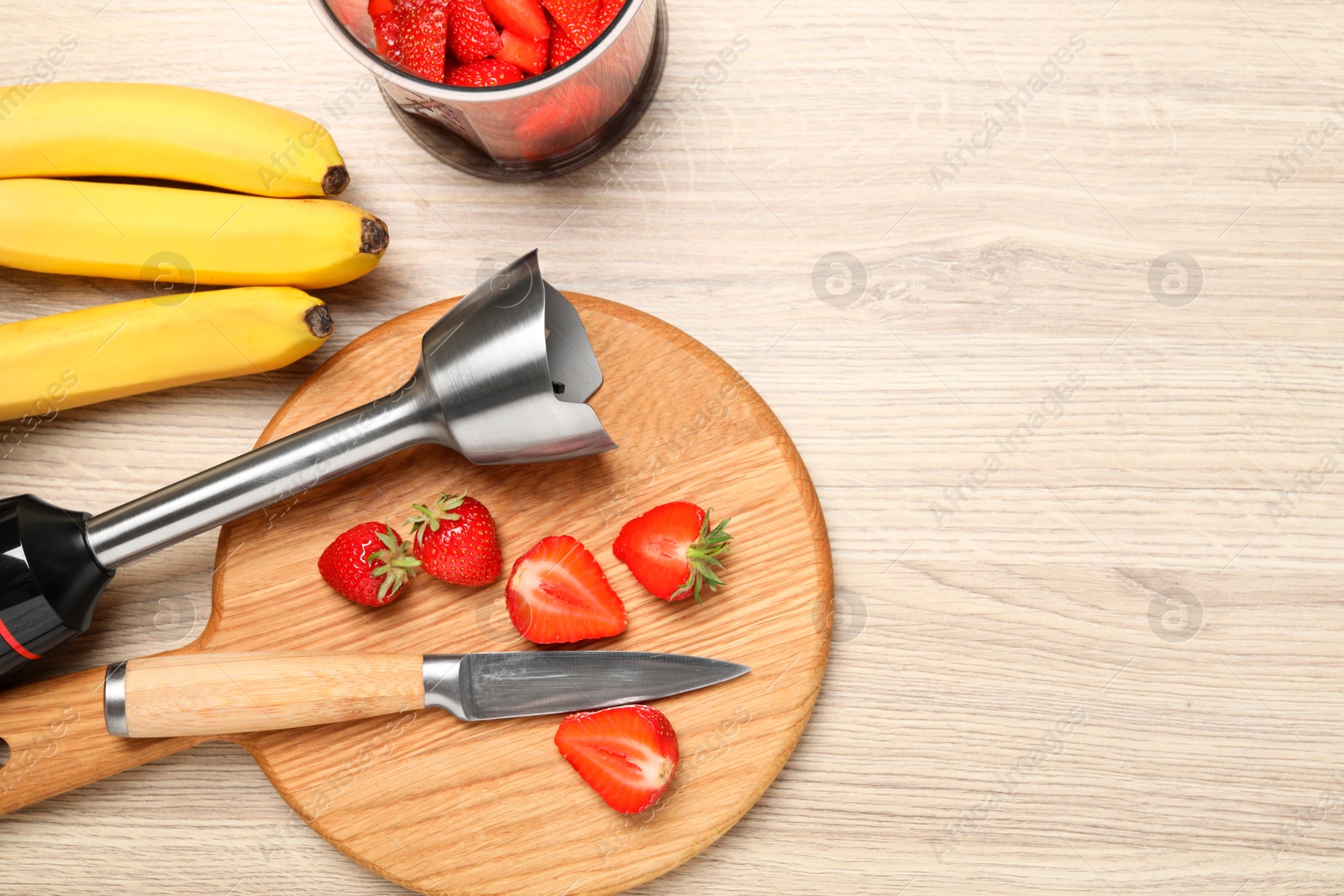 Photo of Hand blender kit, fresh bananas, strawberries and knife on wooden table, flat lay. Space for text