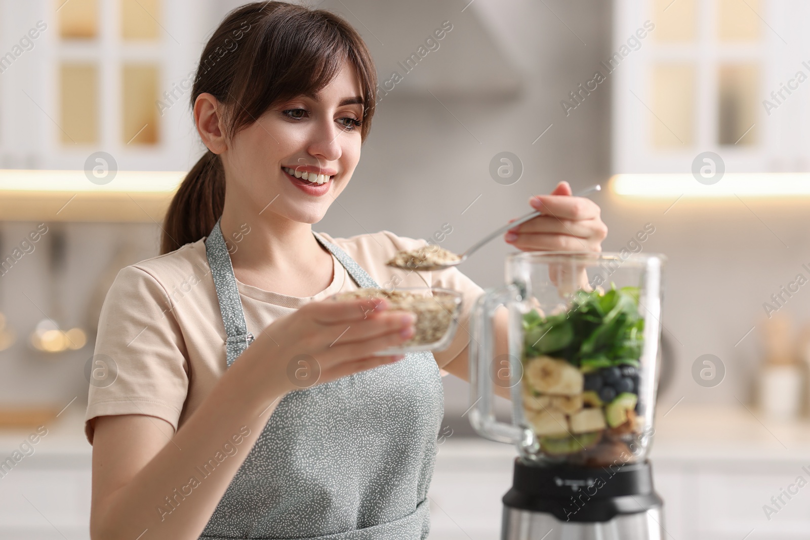 Photo of Young woman making delicious smoothie with blender in kitchen