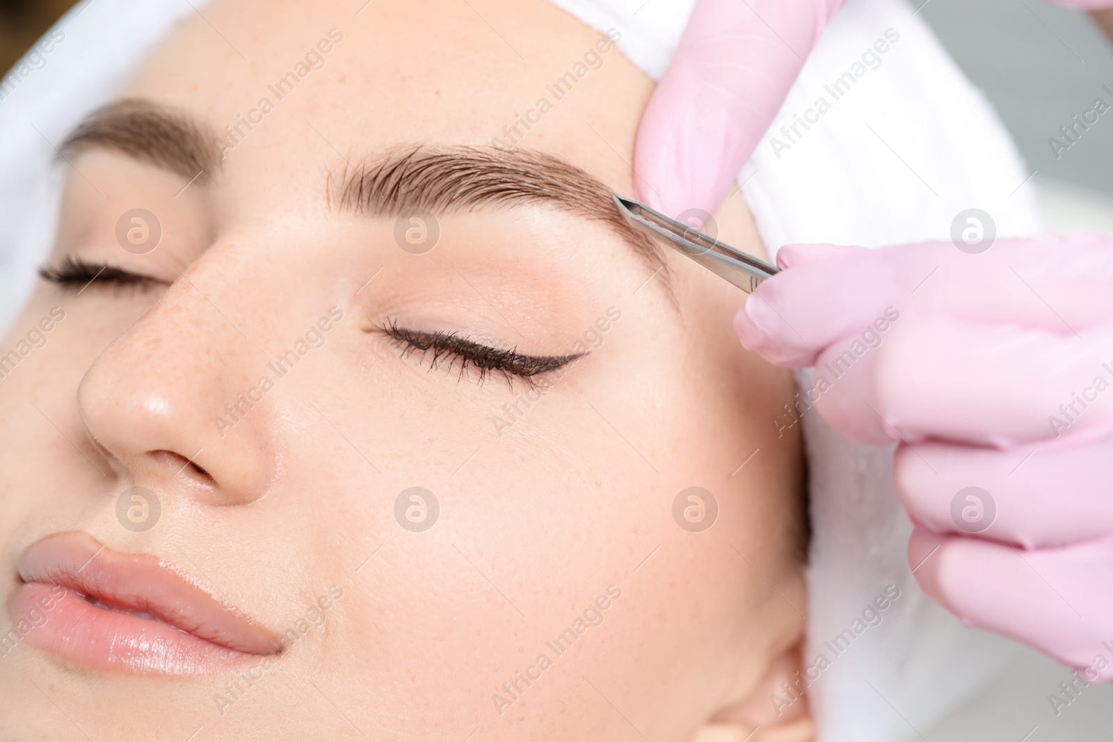 Photo of Beautician plucking young woman's eyebrow in beauty salon, closeup