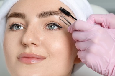 Photo of Beautician making eyebrow correction to young woman in beauty salon, closeup