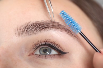 Photo of Beautician making eyebrow correction to young woman, closeup