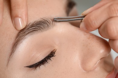 Photo of Beautician plucking young woman's eyebrow, closeup view