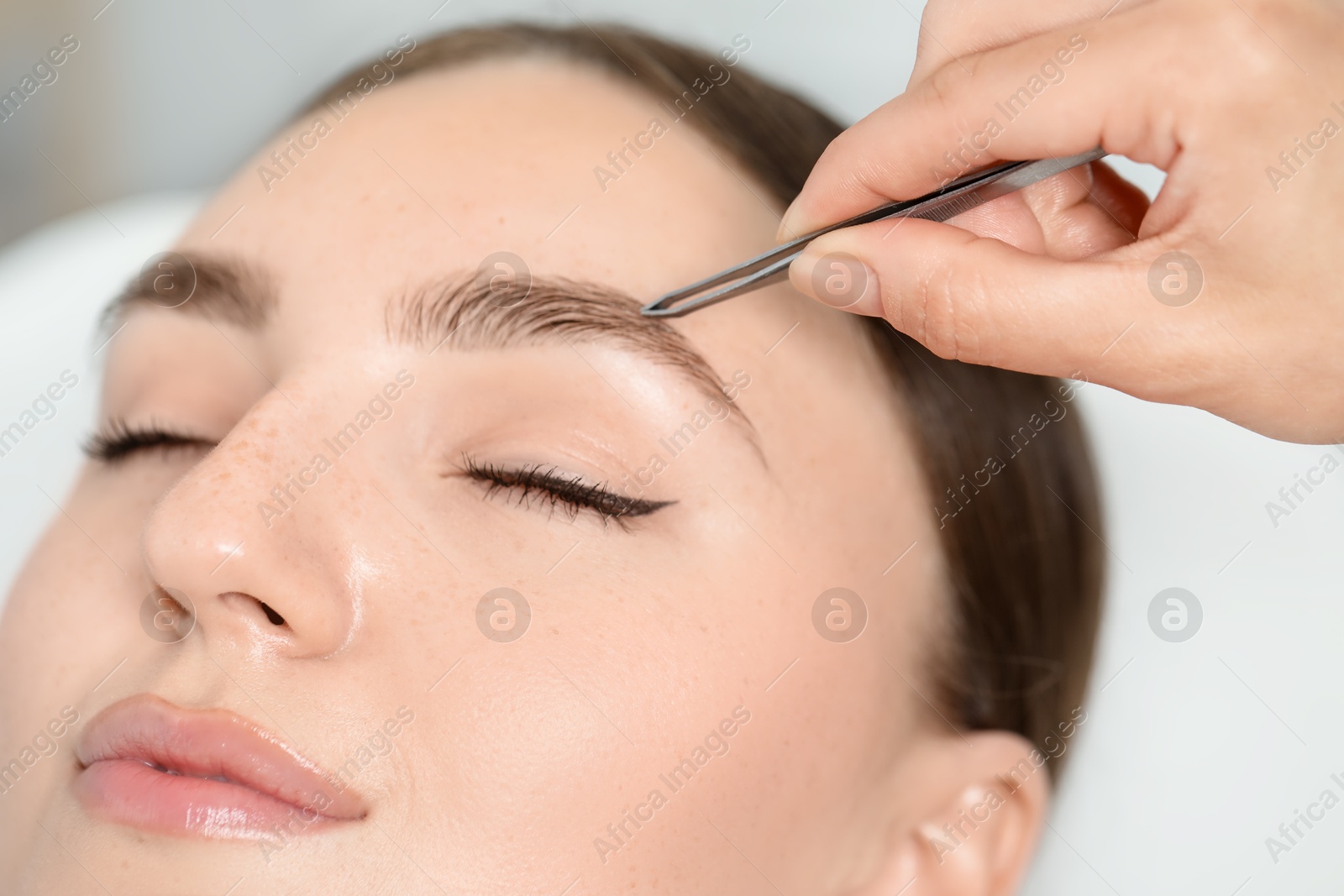 Photo of Beautician plucking young woman's eyebrow in beauty salon, closeup