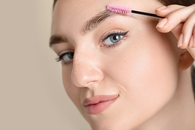 Photo of Young woman with spoolie brush on beige background, closeup. Eyebrow correction