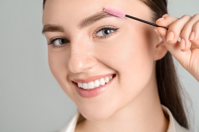 Photo of Young woman with spoolie brush on light background, closeup. Eyebrow correction