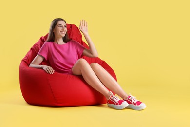 Photo of Smiling woman sitting on red bean bag chair against yellow background