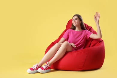 Photo of Smiling woman sitting on red bean bag chair against yellow background