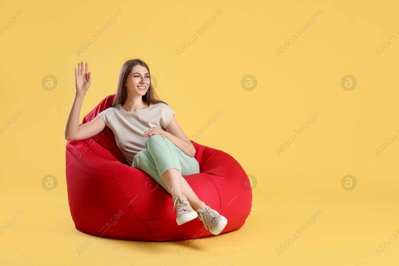 Photo of Smiling woman sitting on red bean bag chair against yellow background, space for text