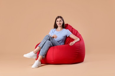 Photo of Smiling woman sitting on red bean bag chair against beige background