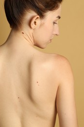 Photo of Woman with moles on her skin against beige background, back view