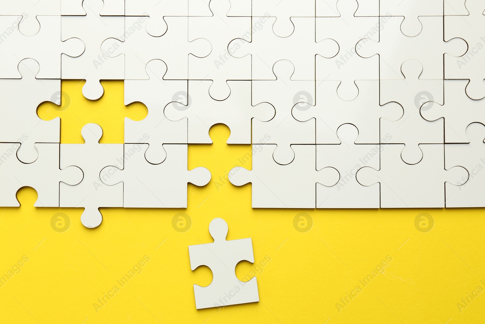 Photo of White puzzle pieces on yellow background, top view