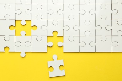 Photo of White puzzle pieces on yellow background, top view