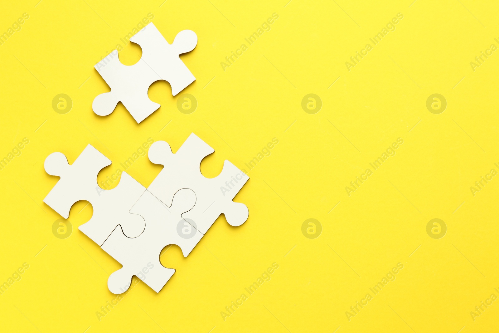 Photo of White puzzle pieces on yellow background, top view. Space for text