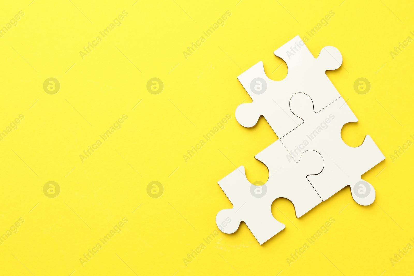 Photo of White puzzle pieces on yellow background, top view. Space for text