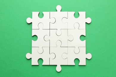 Photo of White puzzle pieces on green background, top view