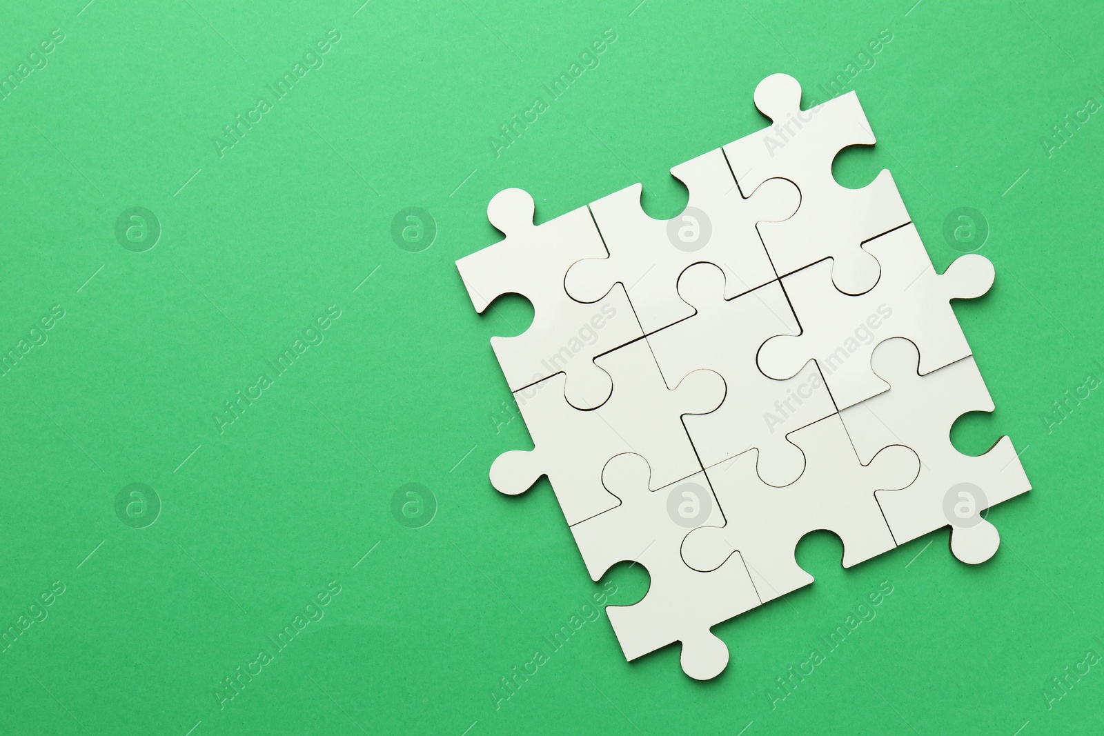 Photo of White puzzle pieces on green background, top view. Space for text