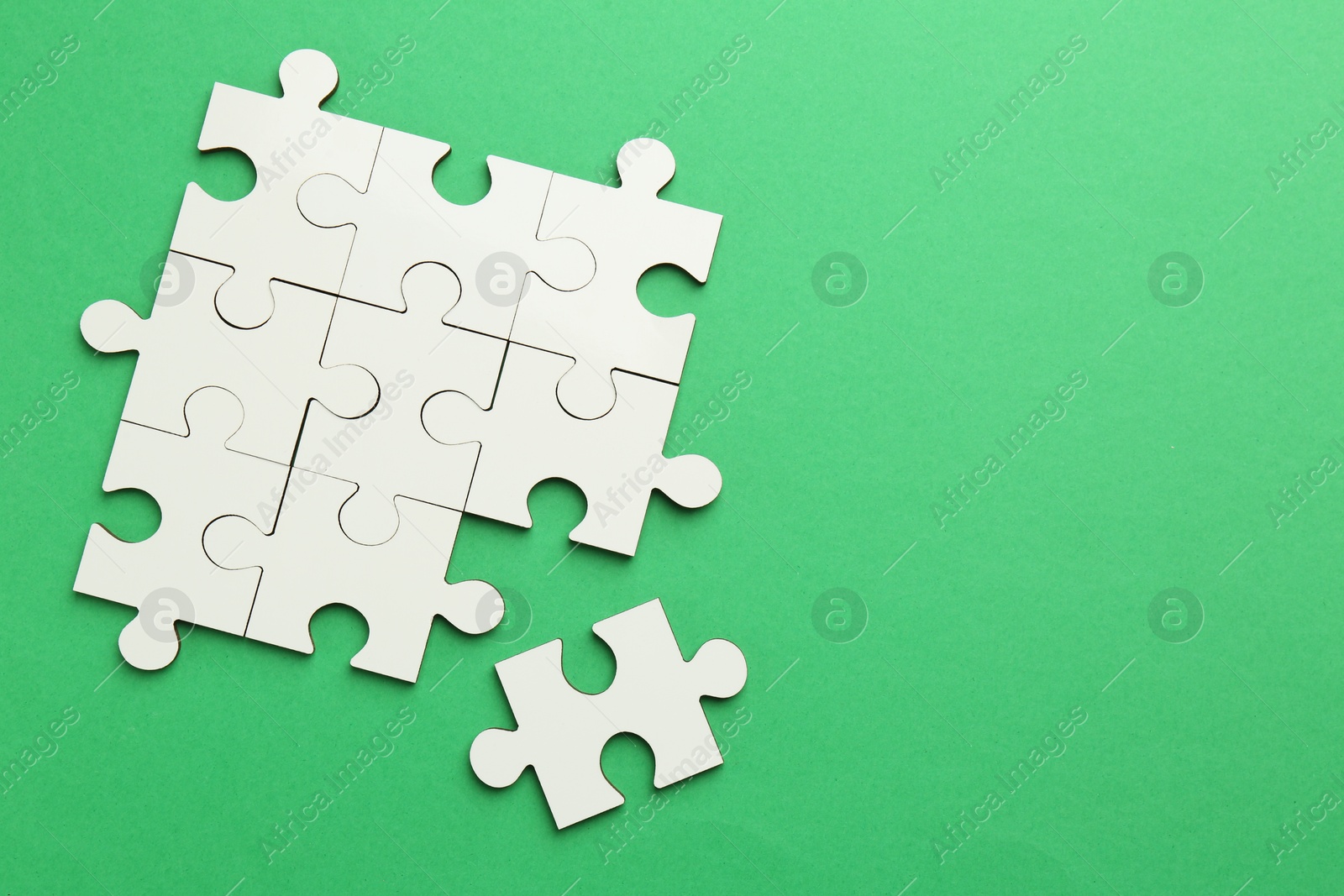 Photo of White puzzle pieces on green background, top view. Space for text