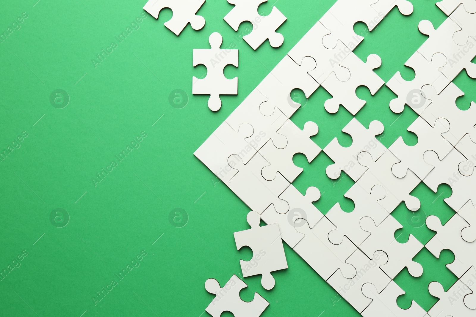 Photo of White puzzle pieces on green background, top view. Space for text