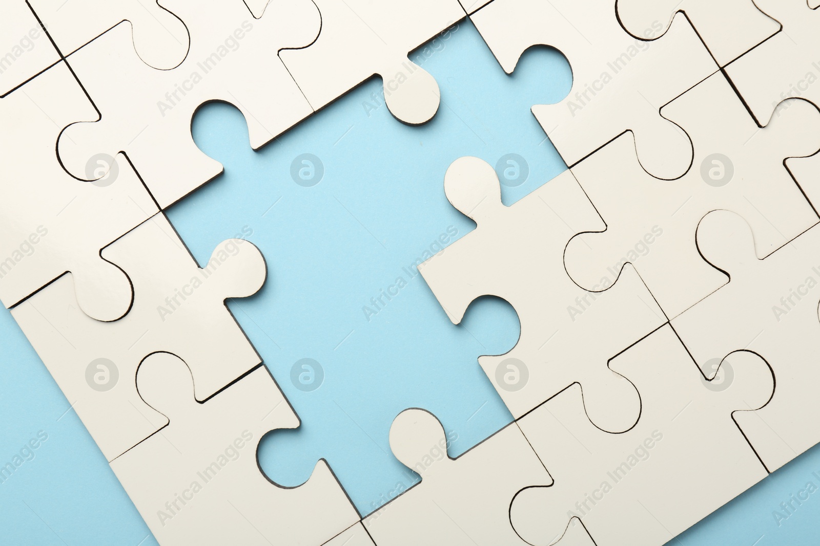 Photo of White puzzle with missing pieces on light blue background, top view