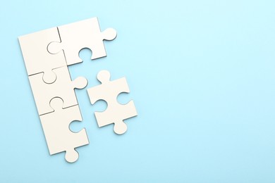 Photo of White puzzle pieces on light blue background, top view. Space for text