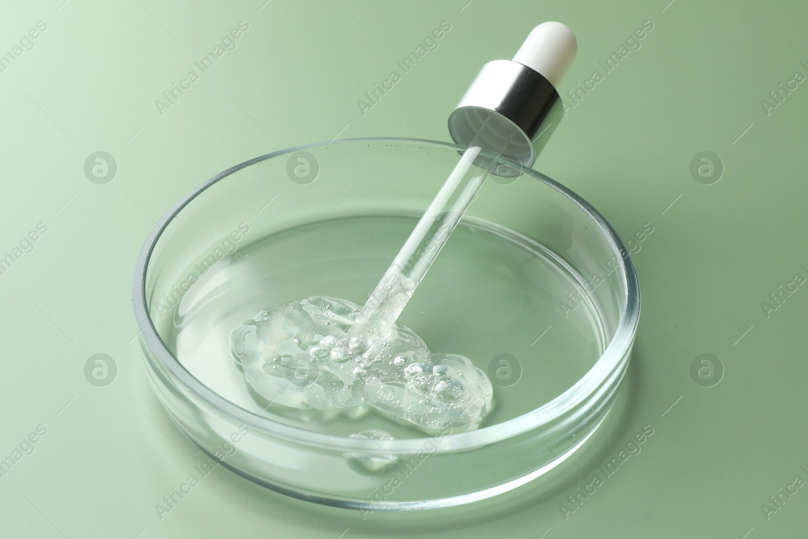 Photo of Petri dish with cosmetic product and pipette on green background, closeup