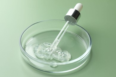 Petri dish with cosmetic product and pipette on green background, closeup