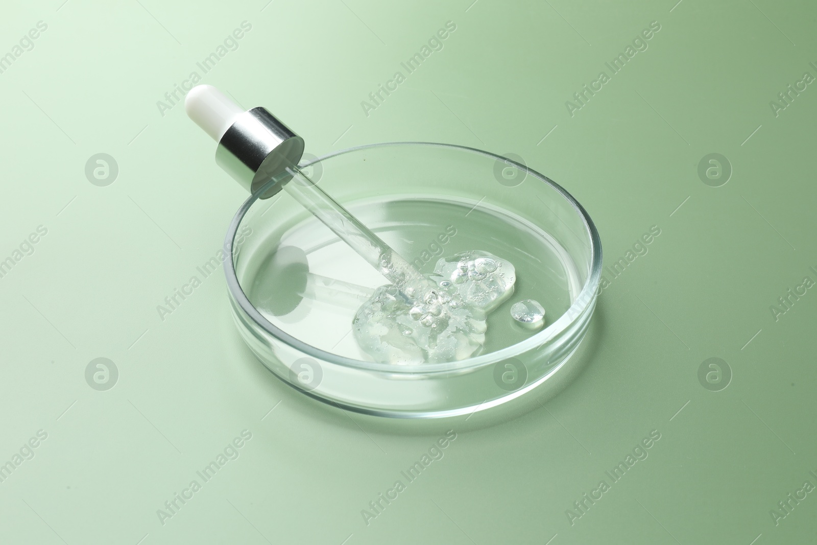 Photo of Petri dish with cosmetic product and pipette on green background