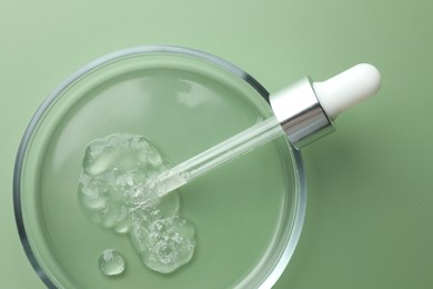 Photo of Petri dish with cosmetic product and pipette on green background, top view