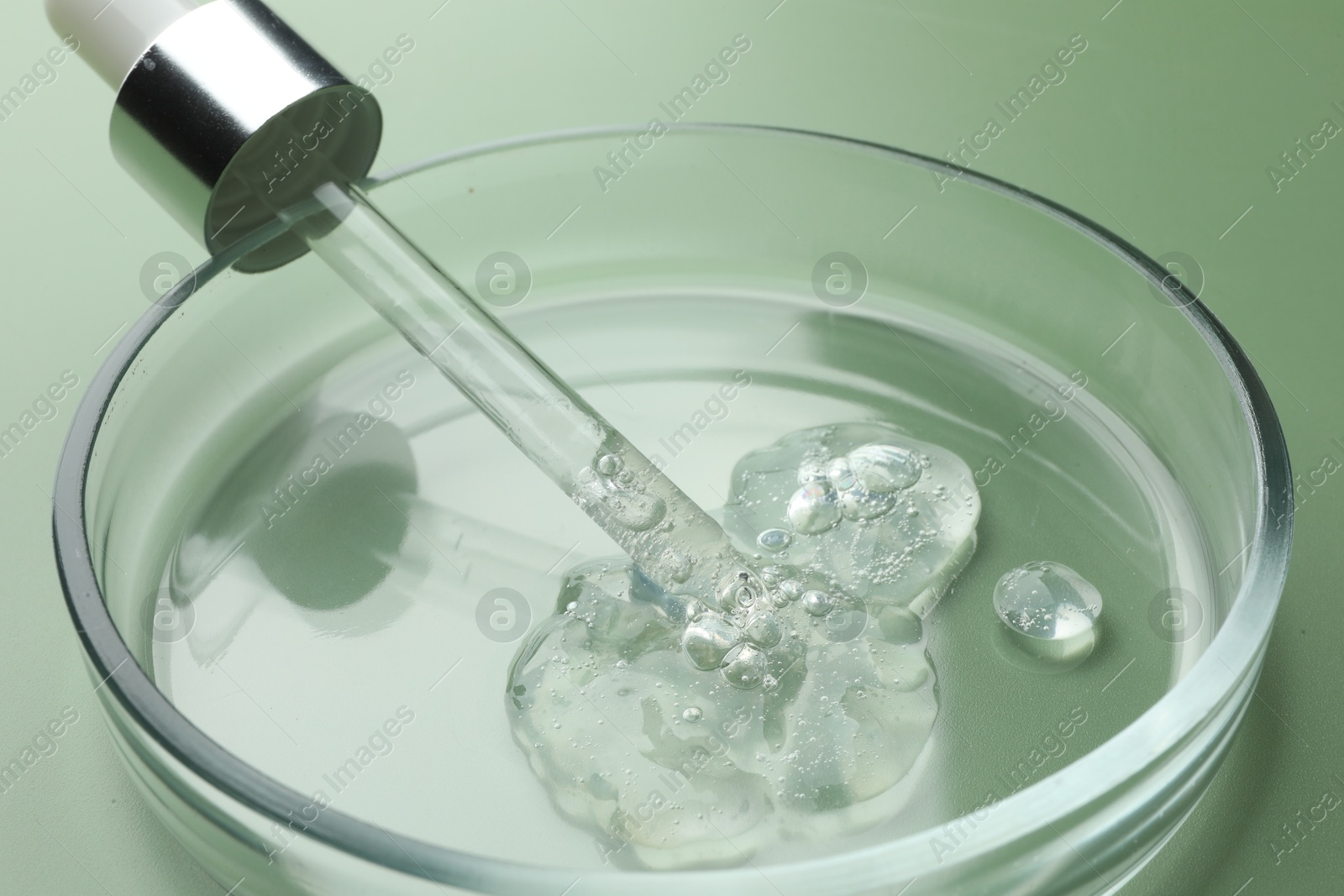 Photo of Petri dish with cosmetic product and pipette on green background, closeup