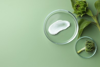 Petri dishes with cosmetic product and sunflowers on green background, flat lay. Space for text