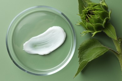 Petri dish with cosmetic product and sunflower on green background, flat lay