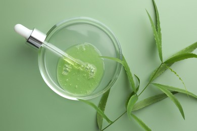 Petri dish with cosmetic product, pipette and leaves on green background, flat lay