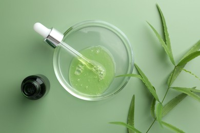 Photo of Petri dish with cosmetic product, bottle, pipette and leaves on green background, flat lay