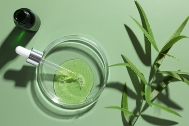 Photo of Petri dish with cosmetic product, bottle, pipette and leaves on green background, flat lay