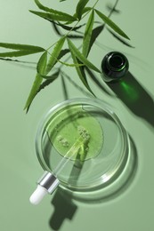 Petri dish with cosmetic product, bottle, pipette and leaves on green background, flat lay