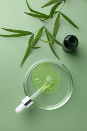 Photo of Petri dish with cosmetic product, bottle, pipette and leaves on green background, flat lay