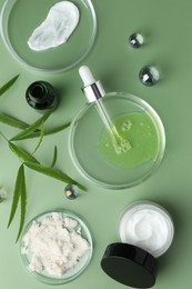 Petri dishes with cosmetic products, pipette and leaves on green background, flat lay